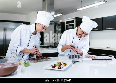 young latin couple woman and man chocolatier in chef uniform and hat preparing mexican chocolates bonbon candies at kitchen in Mexico Latin America Stock Photo
