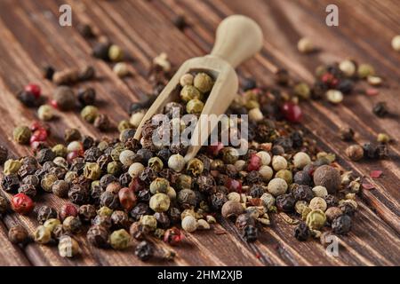 Multicolored pepper mix with wooden spatula scattered over vintage wooden background Stock Photo