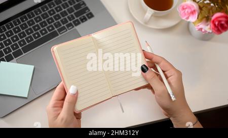 Top view of open school notebook with blank pages in women's hands over modern office desk. Feminine workspace Stock Photo
