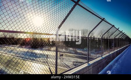 Looking over the bridge from behind the chain-link fence. Snow covers the sidewalk and the highway under the clear blue sky. Stock Photo