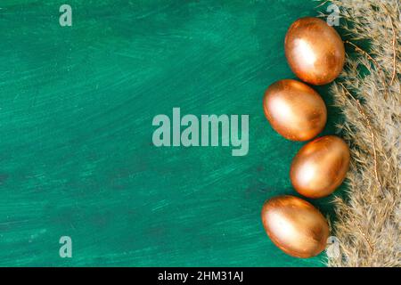 Golden Easter eggs and golden branches, reeds on a green watercolor background. Banner. Layflat. Space for text Stock Photo