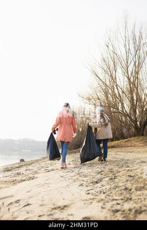 Two volunteers picking up trash from the beach Stock Photo