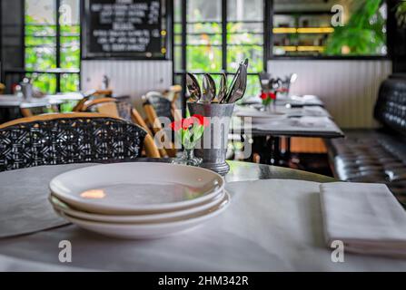 Art deco and colonial interior at a cafe with carnation flowers and plates on empty tables, Singapore Stock Photo