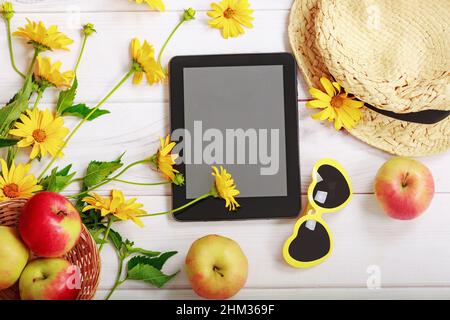 Summer pattern with yellow flowers,  red apples, straw hat, tablet pc and glasses in the shape of a heart. Stock Photo
