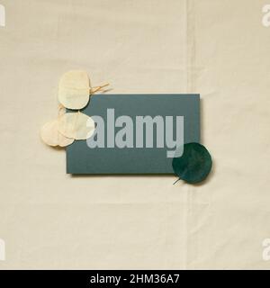 Blank paper sheet card and dry leaf decor on beige fabric background. top view, copy space. minimal invitation template Stock Photo