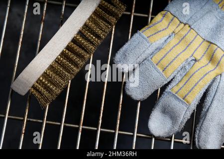 Wire brush and protective glove lying on dirty grill rust. Top view. Stock Photo