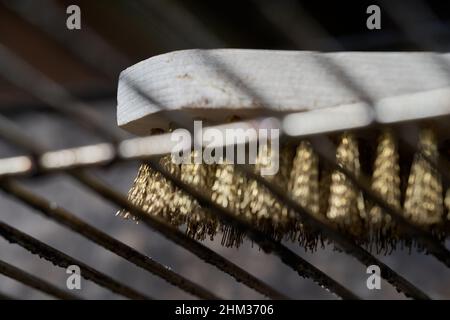 Dirty grill from below, cleaning utensil of brass and wood lies on oily rust. Closeup. Stock Photo