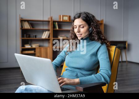 Young pleasant woman in headset using laptop talking with partner via video chat from home Stock Photo