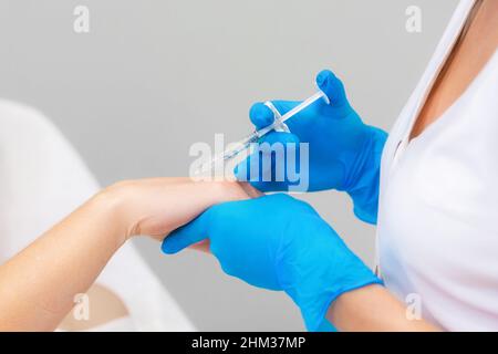 A professional cosmetologist makes an injection into a woman's hand. Botulinum therapy in a beauty salon for a client. Close-up. Stock Photo