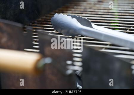 Part of a stainless steel grill tongs on a dirty grill rust. Wooden handle blurred in the foreground. Side view. Depth of field. Stock Photo