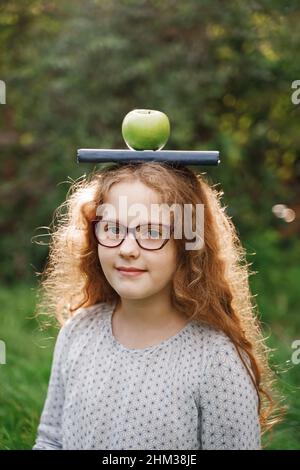 Laughing girl with a book and apple on his head. Easy learning concept. Stock Photo