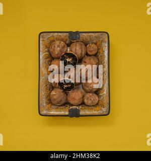 Sun dried organic Loomi or Black Lime, Black Lemon, Omani Lemon in antiquarian oriental plate on yellow background.  Stock Photo