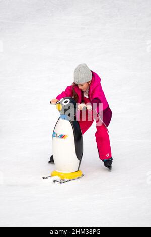 Lone little girl learning to skate on ice using ski penguin ice skating aid Stock Photo