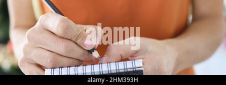 Female waiter writing down ordered dishes in notebook with pencil closeup Stock Photo