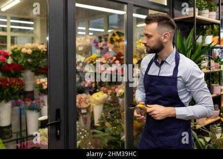 an employee of a flower shop with coffee in his hands against the background of a refrigerator with bouquets Stock Photo