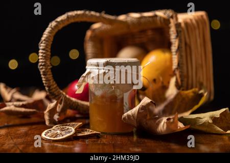 A jar of peach jam with slices of dried orange with an overturned wicker basket and dry leaves in the background Stock Photo
