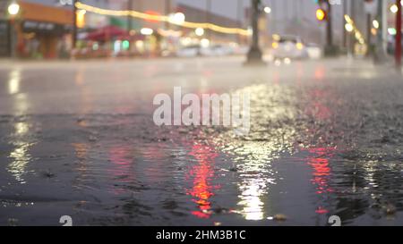 Cars lights reflection on road in rainy weather. Rain drops on wet asphalt of city street in USA, raindrops falling on sidewalk. Puddle of water on pavement. Torrential downpour or rainfall at night. Stock Photo