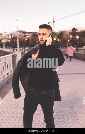 Young caucasian man using a smartphone at Donostia-San Sebastian sea walk during sunset time. Stock Photo