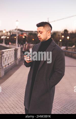 Young caucasian man using a smartphone at Donostia-San Sebastian sea walk during sunset time. Stock Photo