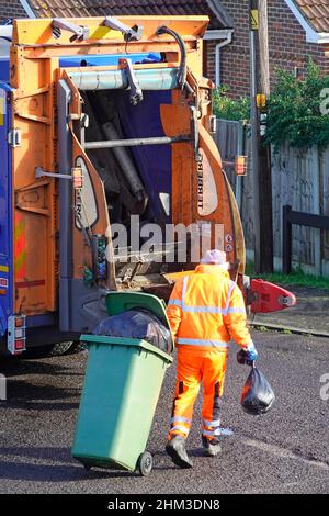 Dustman refuge collector back view in high visibility clothing pulling wheelie bin full of black rubbish sacks into lorry truck council dustcart UK Stock Photo