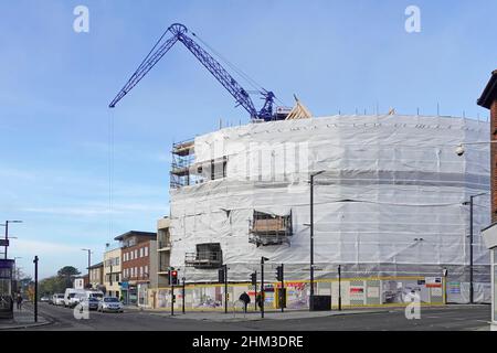 Construction site crane on prime corner plot at busy high street road junction plastic safety cocoon around scaffolding & building work Brentwood UK Stock Photo