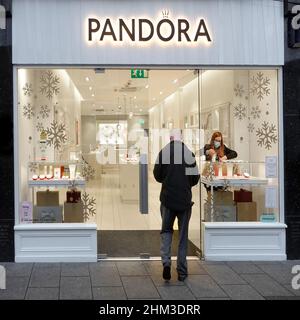Pandora shop front Christmas interior evening lights on view staff employee adjusts window display & back views of male shopper customer outside UK Stock Photo