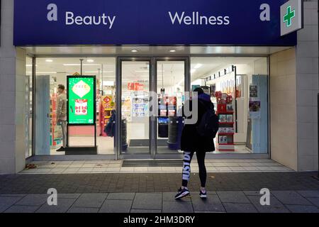 Boots Beauty Wellness store in shopping high street woman customer outside shopfront on pavement a dusk afternoon view at Christmas time England UK Stock Photo