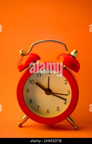 Red round clock on orange table, side view. Stock Photo