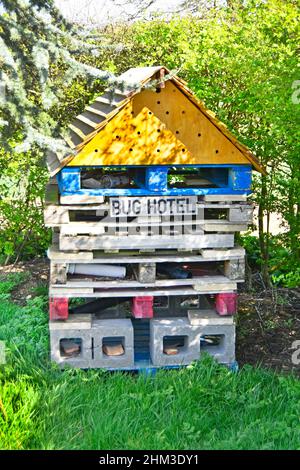 Close up man made Bug Hotel insect house in shady corner of gardeners patch in churchyard cemetery made of timber pallets & concrete blocks England UK Stock Photo