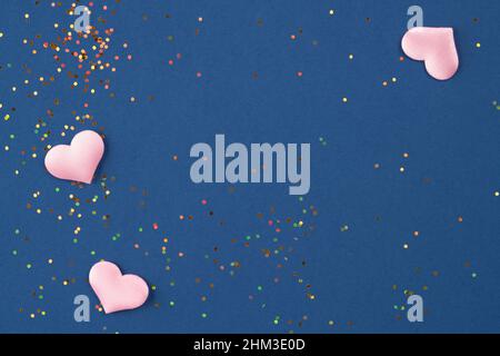 Festive background with pink hearts and small multicolored holographic sparkles on dark blue background with. St.Valentines day background for your pr Stock Photo