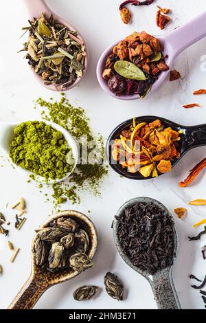 Various types of dry tea in spoons on a white marble background, top view. Green tea, matcha, citrus tea, black tea and herbal detox tea. Stock Photo