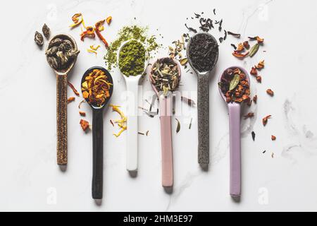 Various types of dry tea in spoons on a white marble background, top view. Green tea, matcha, citrus tea, black tea and herbal detox tea. Stock Photo