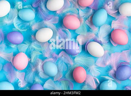 Easter background with colored eggs and feathers on a blue background. Top view. The concept of a Happy Easter. Stock Photo