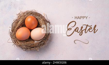 Three eggs of natural color in a nest on a pink background. Top view. The concept of a happy Easter. Stock Photo