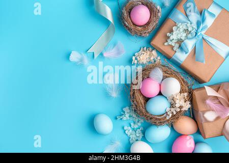 Easter background with colored eggs, nests and gifts on a blue background. Happy Easter. Top view, copy space. Stock Photo