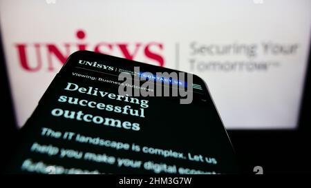 Mobile phone with website of American IT company Unisys Corporation on screen in front of business logo. Focus on top-left of phone display. Stock Photo