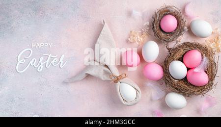 Happy Easter, eggs, nest and Easter bunny made of napkins on a light pink background. Top view. Stock Photo