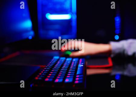 Teenager boy play computer video game in dark room, use neon colored rgb mechanical keyboard, workplace for cybersport gaming Stock Photo