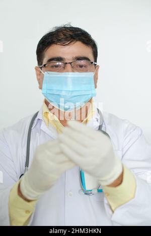 Portrait of concentrated mature doctor in medical mask holding syringe with vaccine against contagious disease Stock Photo