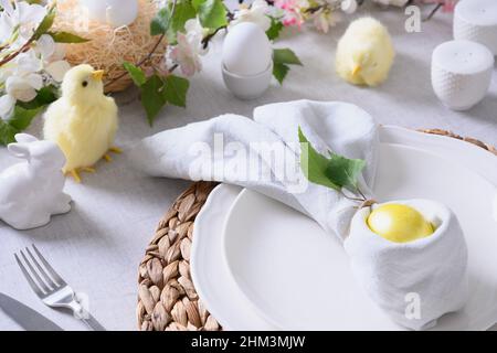 Easter table setting and dinner with yellow chick, festive decorations, fresh flowers and eggs. Close up. Stock Photo