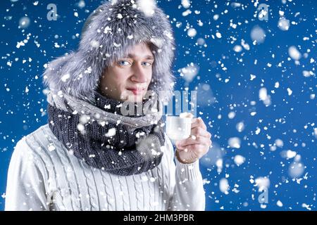 Winter time. The room is cool. A man in a hat and a scarf holds a cup with a drink. The blonde gets warm from the cold with hot coffee or tea. Keep aw Stock Photo
