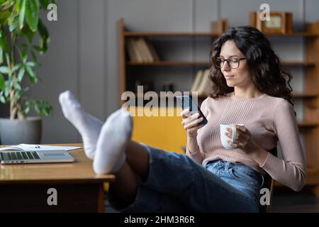 Woman freelancer procrastinate from work. Female distracted from laptop scroll social media on phone Stock Photo