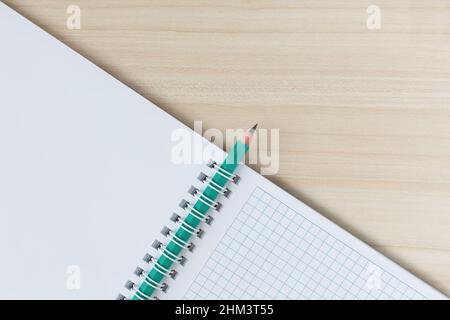 A pencil inserted into a spiral clip of a notepad, on a wooden table,diagonally. Top view Stock Photo