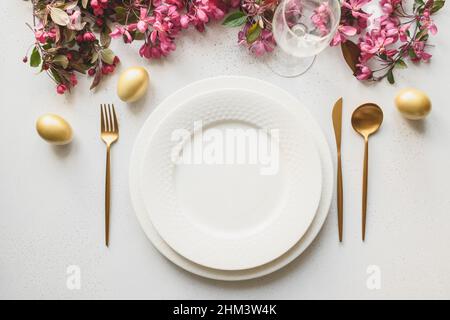 Easter festive dinner with golden eggs, festive tableware and flowers on white background. Top view. Festive tablescapes. Stock Photo