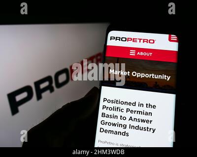 Person holding cellphone with webpage of US oilfield company ProPetro Holding Corp. on screen in front of logo. Focus on center of phone display. Stock Photo