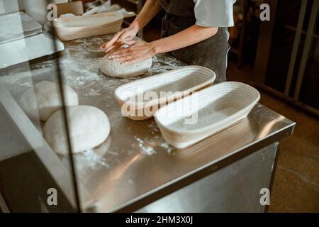 Employee kneads dough for bread at table with dishes in craft bakery Stock Photo