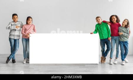 Happy Diverse Kids Standing Near White Board Over Gray Background Stock Photo