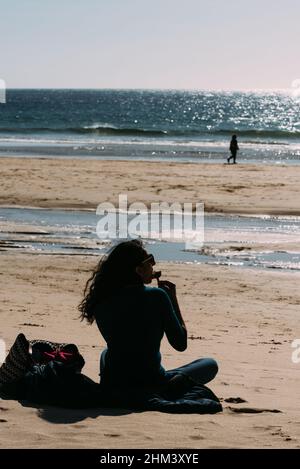 Carcavelos Beach, Portugal - February 5, 2022: Young woman enjoys an ice cream on a sunny winter day at Carcavelos beach in Lisbon Region, Portugal Stock Photo