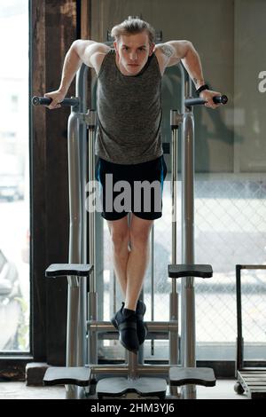Fit young man doing exercise on pull-up machine when working out of triceps Stock Photo