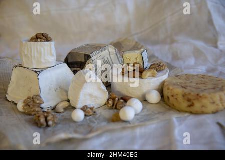 Various types of cheese with sweets and nuts on wrapping paper on a light background. Home production, natural products. Stock Photo